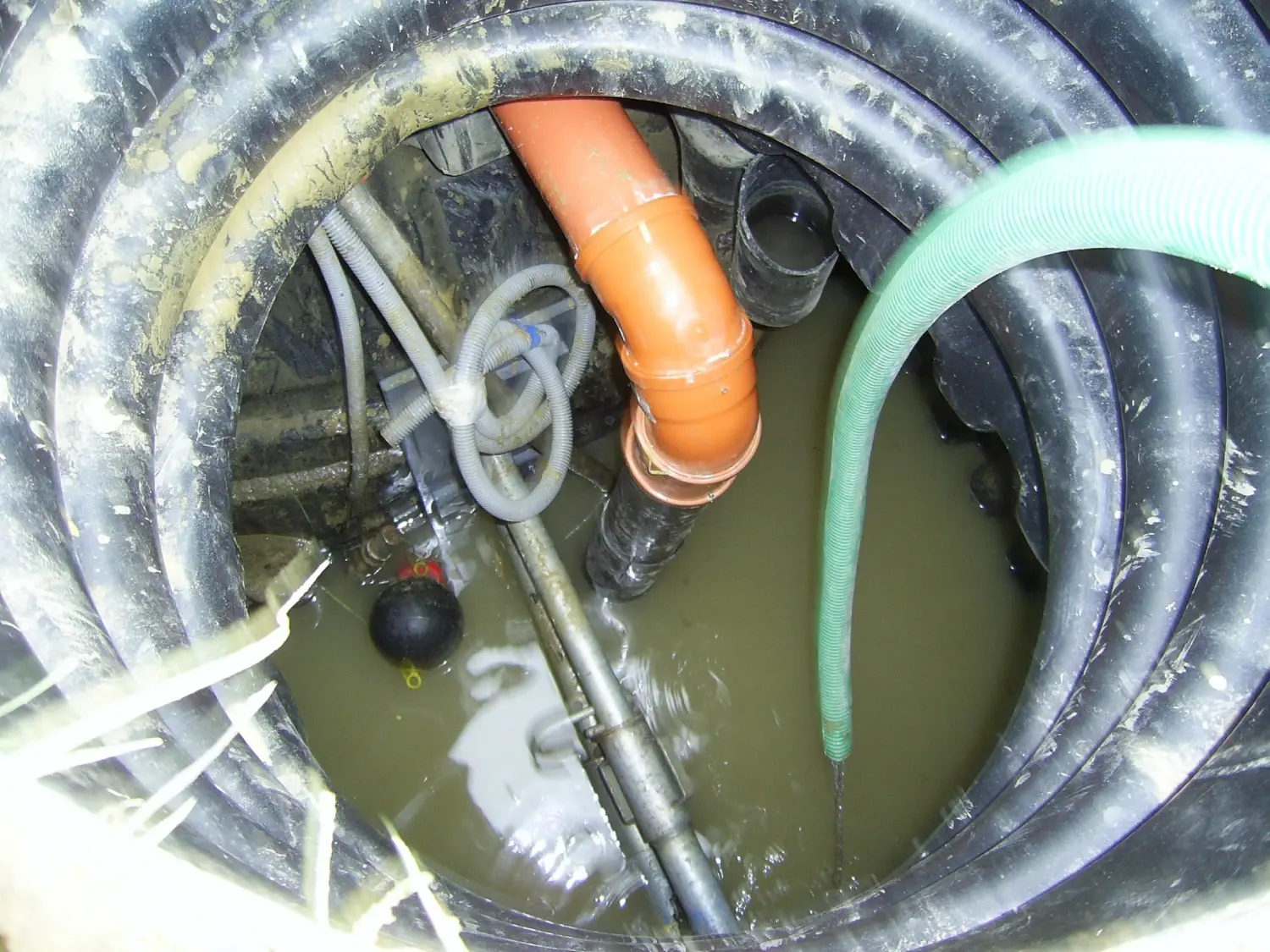Looking down a duct shaft with pipes, hoses and standing water